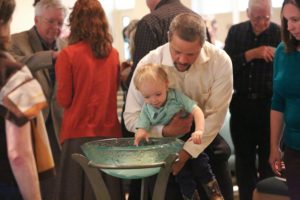 Father lifting son to place their pledge in the baptismal font